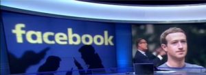 Facebook CEO Mark Zuckerberg sits in front of a Facebook backdrop.
