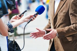A microphone is pointed at a man. We only see his outreached hands and the hands of the person holding the mic.
